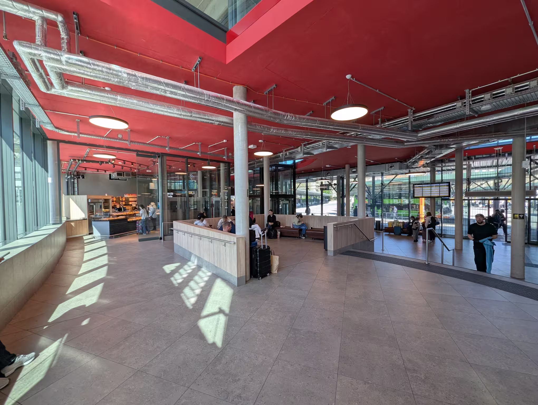 An interior shot of the waiting hall with a seating area, arrival board, and a glass front