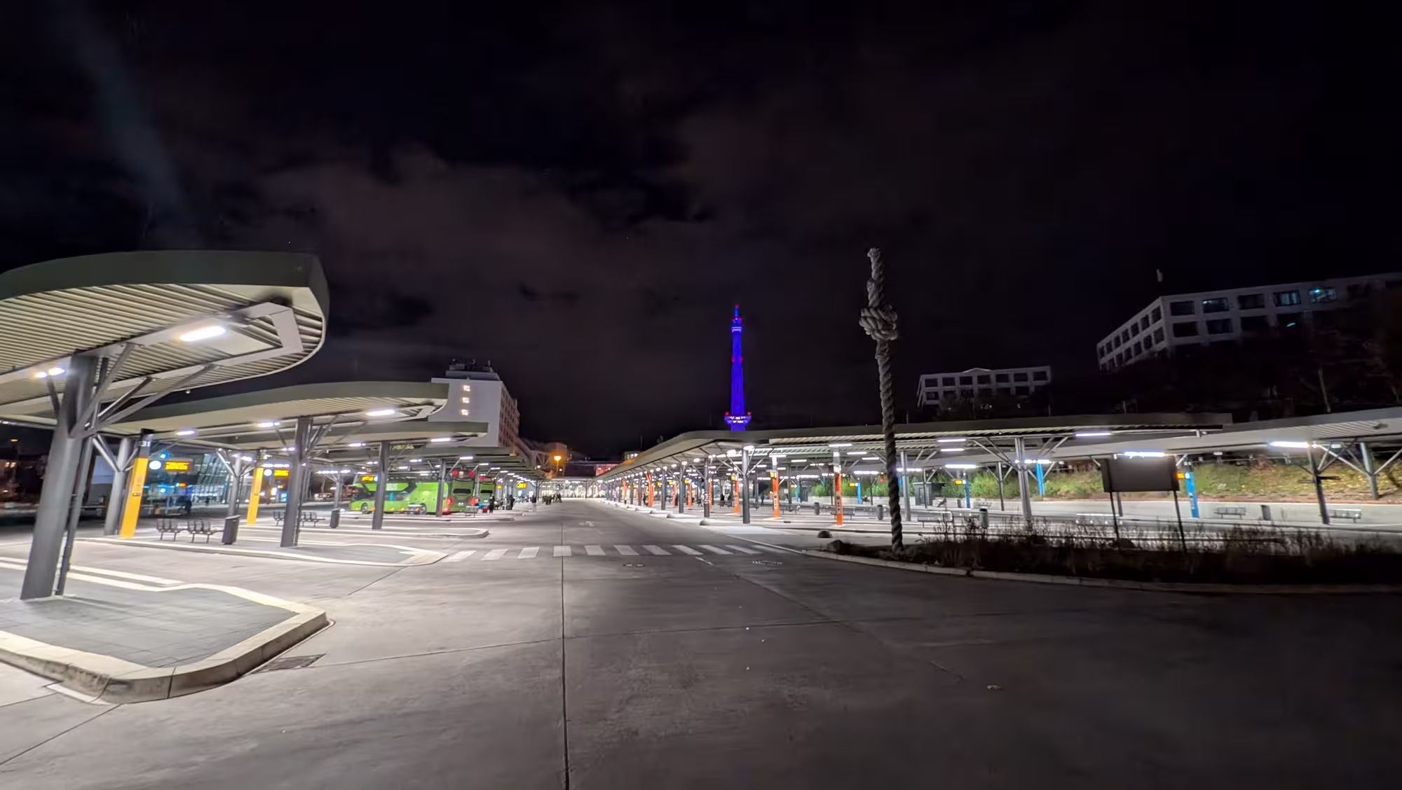 The illuminated central bus station (ZOB) stops at night with a view of the blue-lit radio tower
